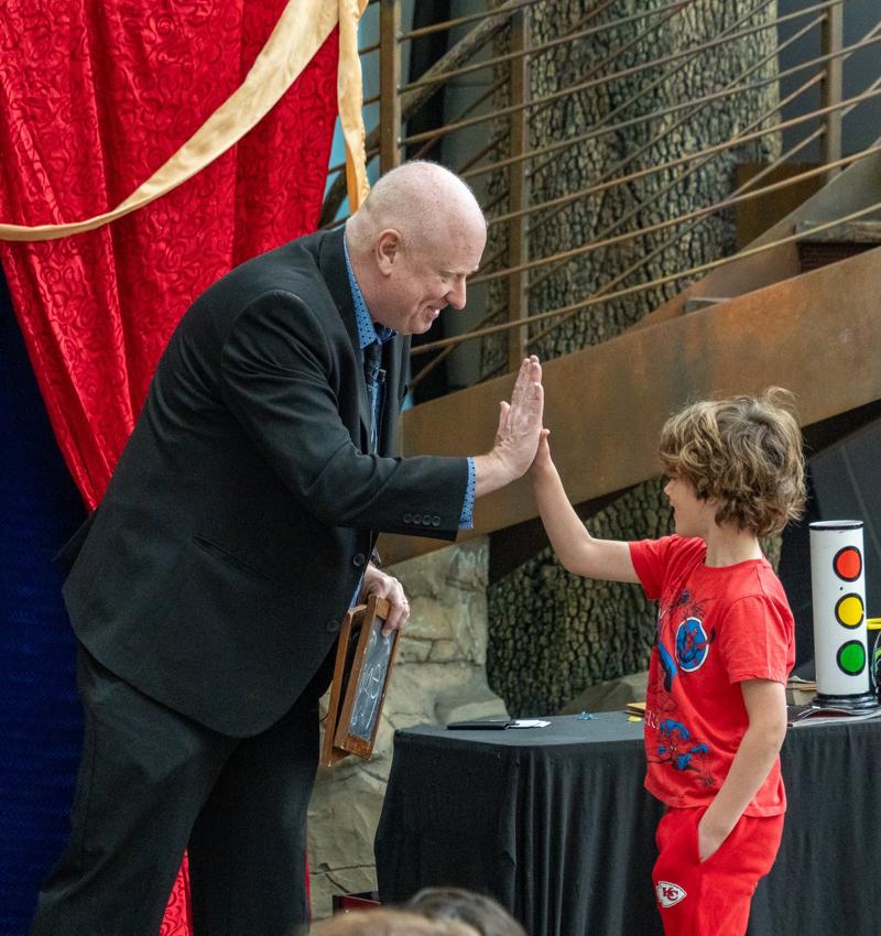 Scott Henderson high-fiving a young audience volunteer in a Kansas City Chiefs shirt at Science City, Union Station