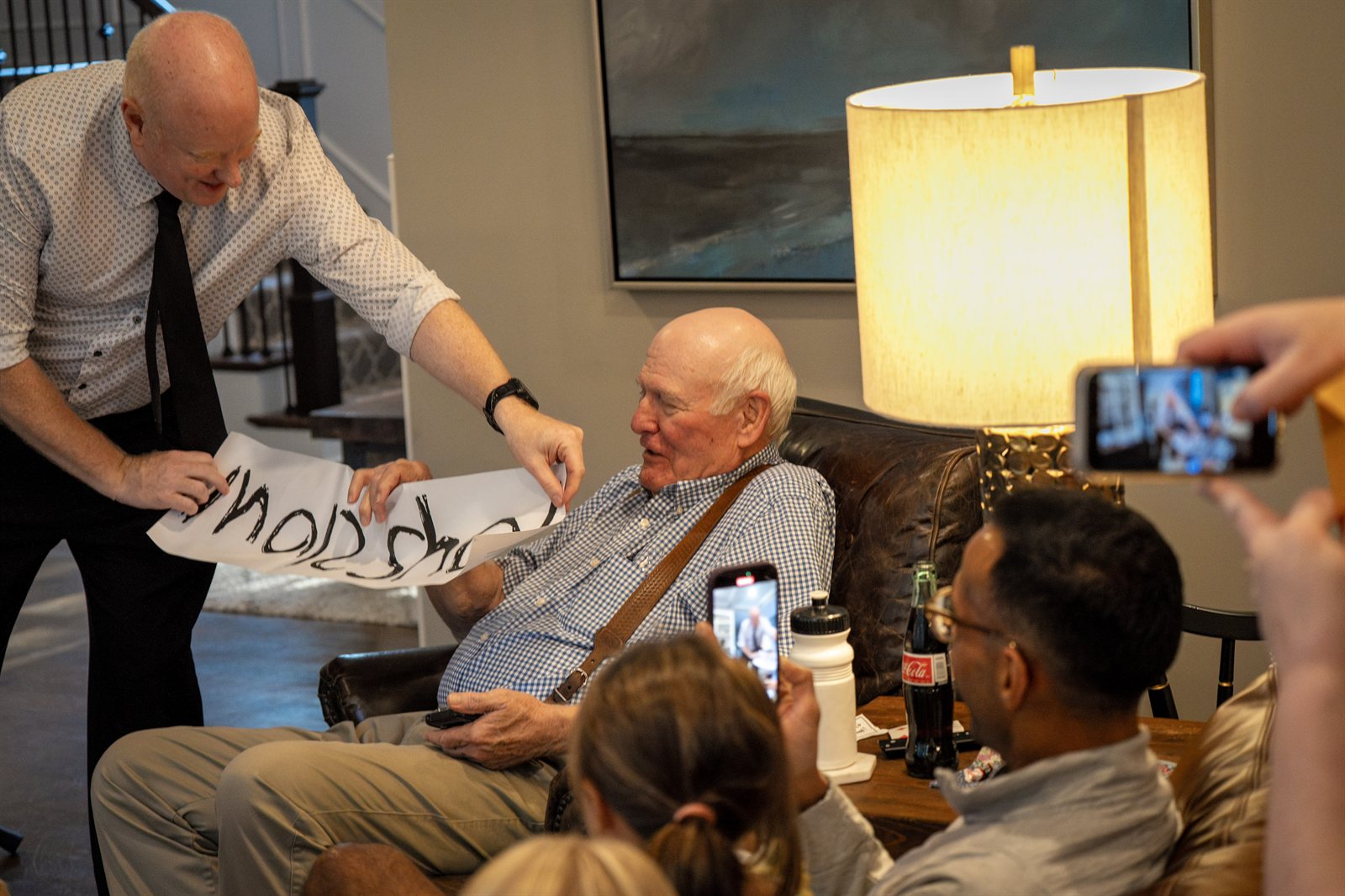 Magic Scott handing an older guest a hand-lettered prediction at a corporate close-up event in Kansas City — phones up, lamp-lit room, guests filming the reveal