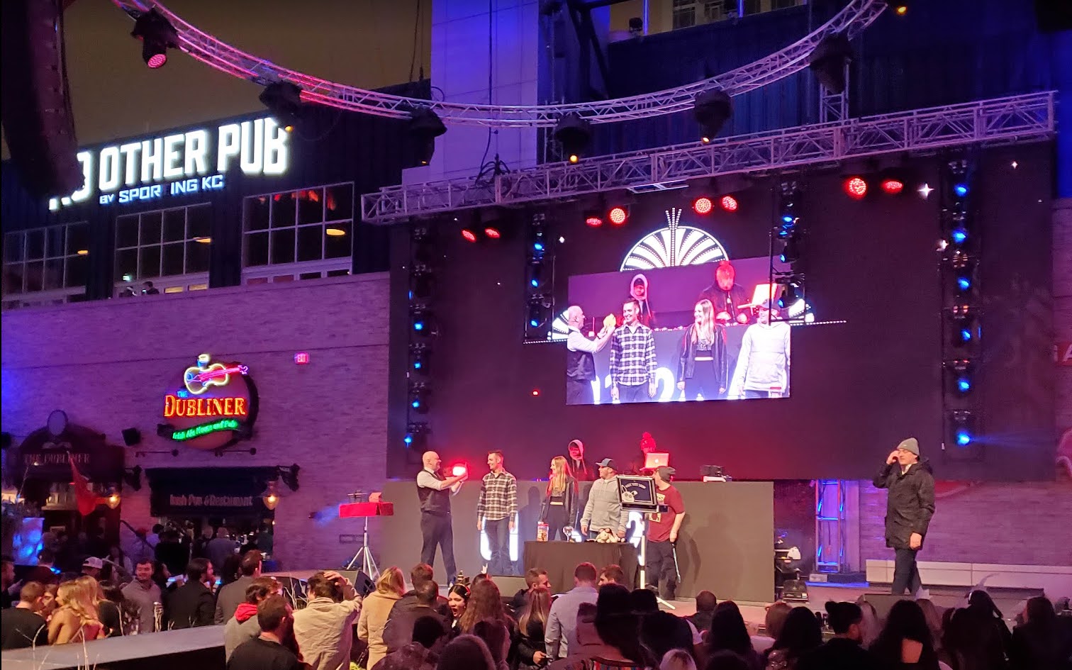 Scott Henderson on the outdoor stage at Power & Light's KC Live! Block, four volunteers beside him, the moment mirrored on a jumbotron above a crowd of thousands.